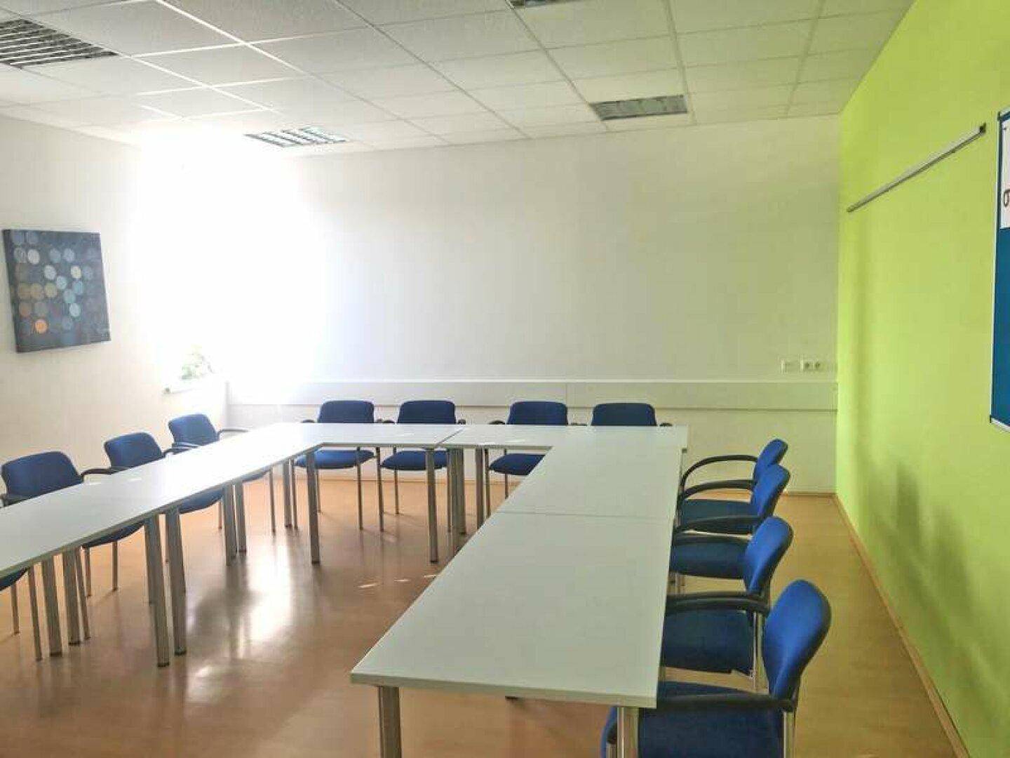 Geräumiger Konferenzraum mit U-förmiger Tischordnung und blauen Stühlen, ideal für Schulungen und Besprechungen.