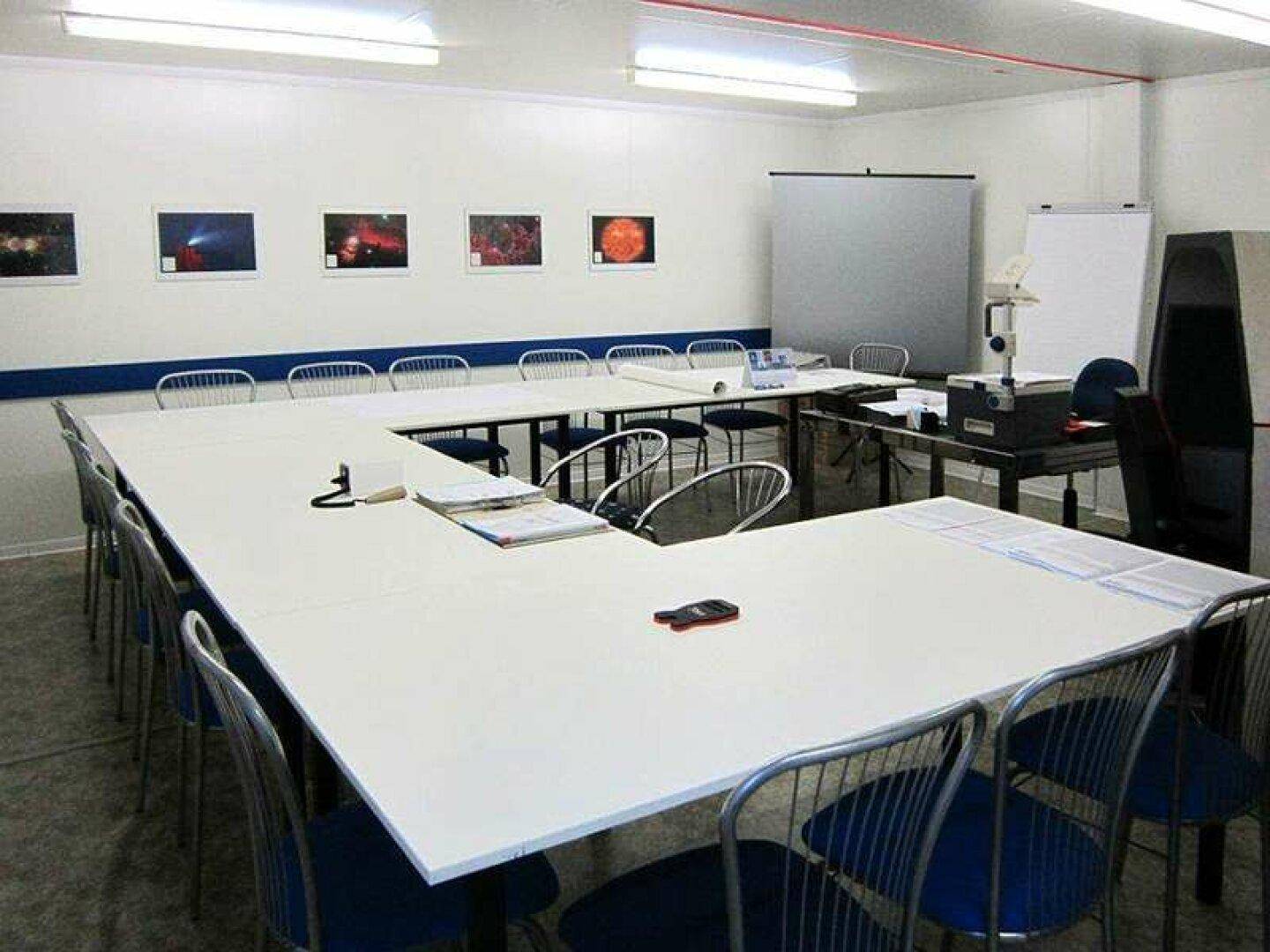 Geräumiger Konferenzraum mit einem großen U-förmigen Tisch, vielen Stühlen und Bildern an den Wänden.