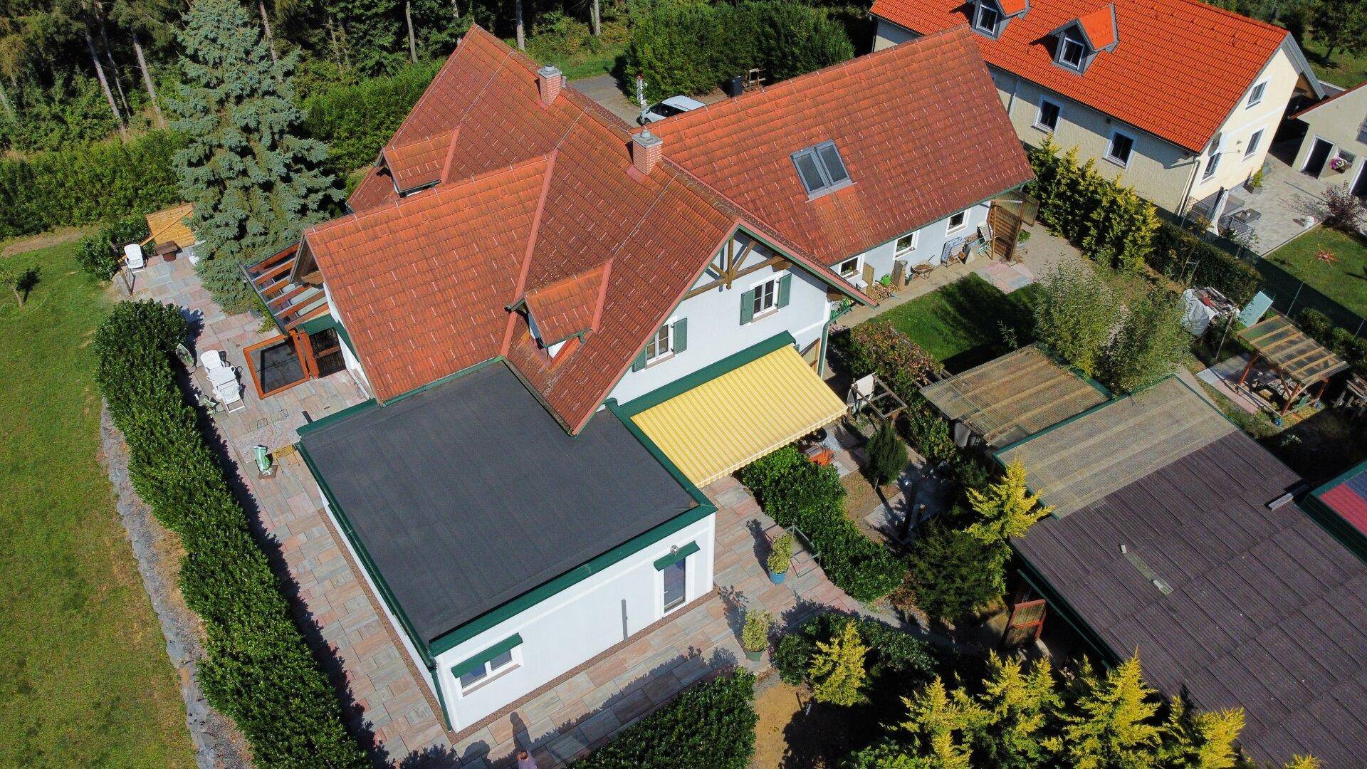 Luftaufnahme des Hauses mit großem Gartenbereich, Terrasse und angrenzendem Waldstück.