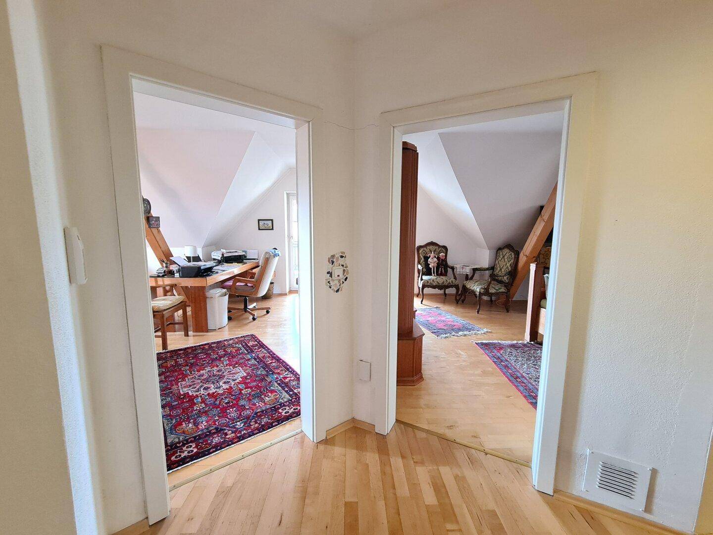 Heller Flur mit Holzparkettboden, der zu zwei Zimmern mit Dachschrägen führt.