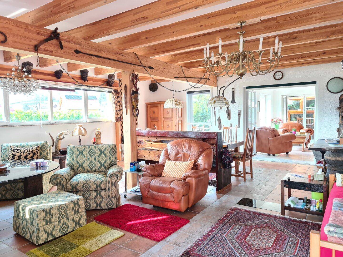Rustikaler Wohn- und Essbereich mit Holzbalkendecke, Ledersesseln und traditionellen Teppichen.