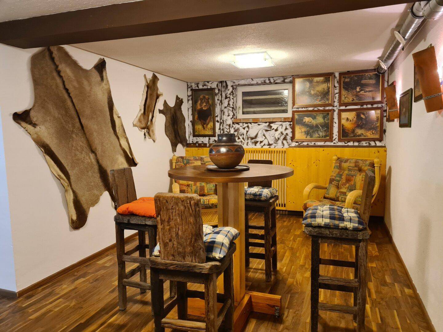 Rustikaler Kellerraum mit Holzboden, Barhockern und Tierfellen als Wanddekoration.