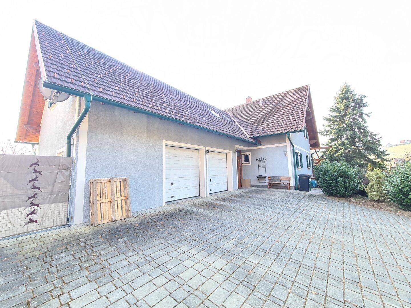 Vorderansicht des Hauses mit Doppelgarage, gepflasterter Einfahrt und umgebender Bepflanzung.