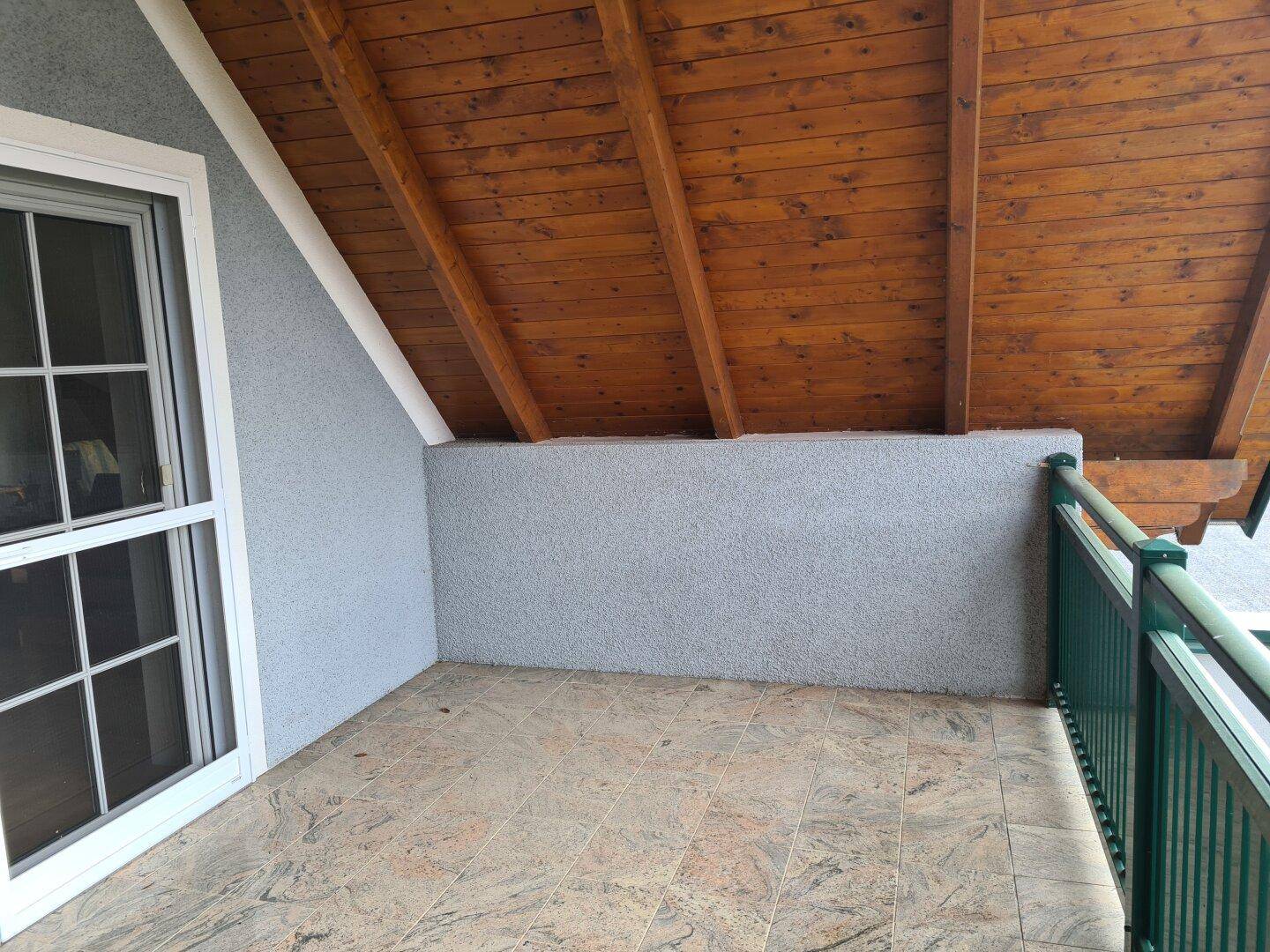 Überdachter Balkon mit Fliesenboden, Holzdecke und grünem Geländer.