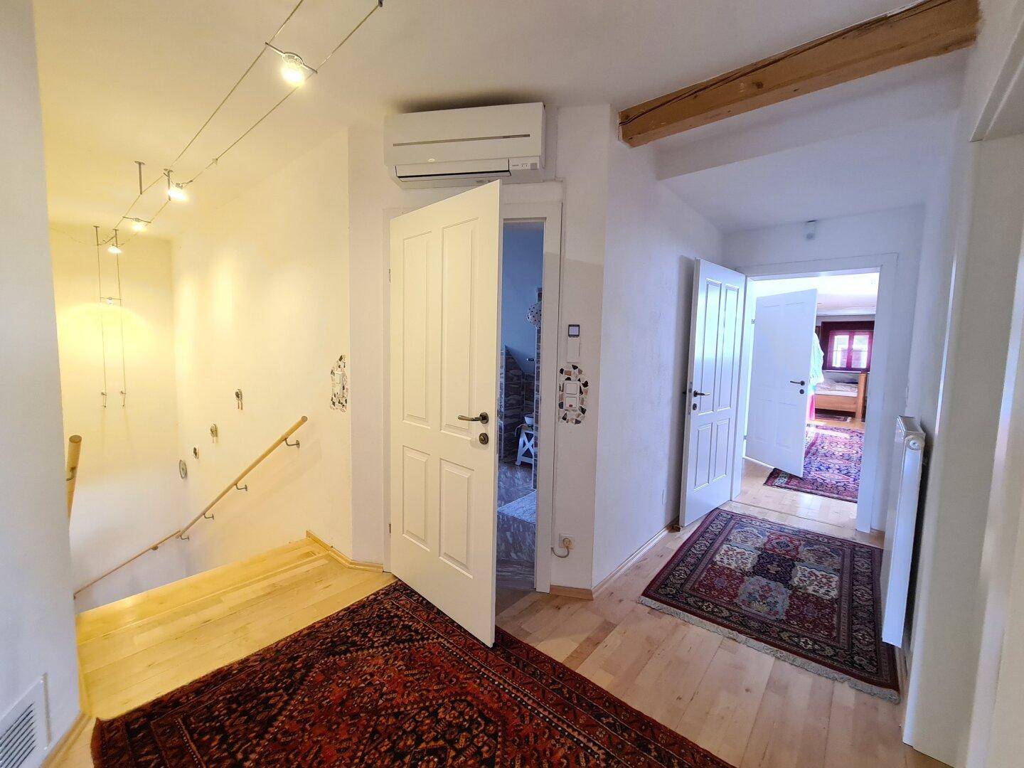 Eingangsbereich mit Holztreppe, Parkettboden und einer Klimaanlage an der Wand.