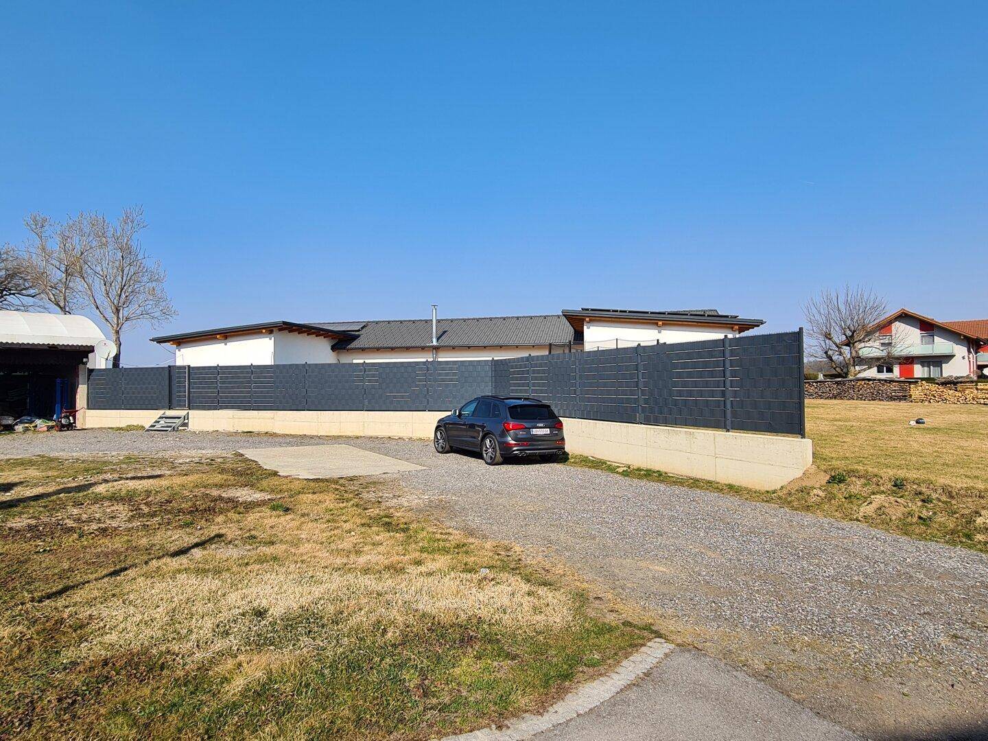Außenbereich mit Kiesauffahrt, Zaun und einem geparkten Auto vor einem Gebäude.