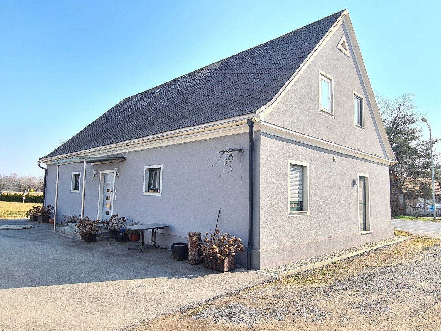 Ansicht des Hauses von der Seite mit Satteldach, grauer Fassade und Fenstern.