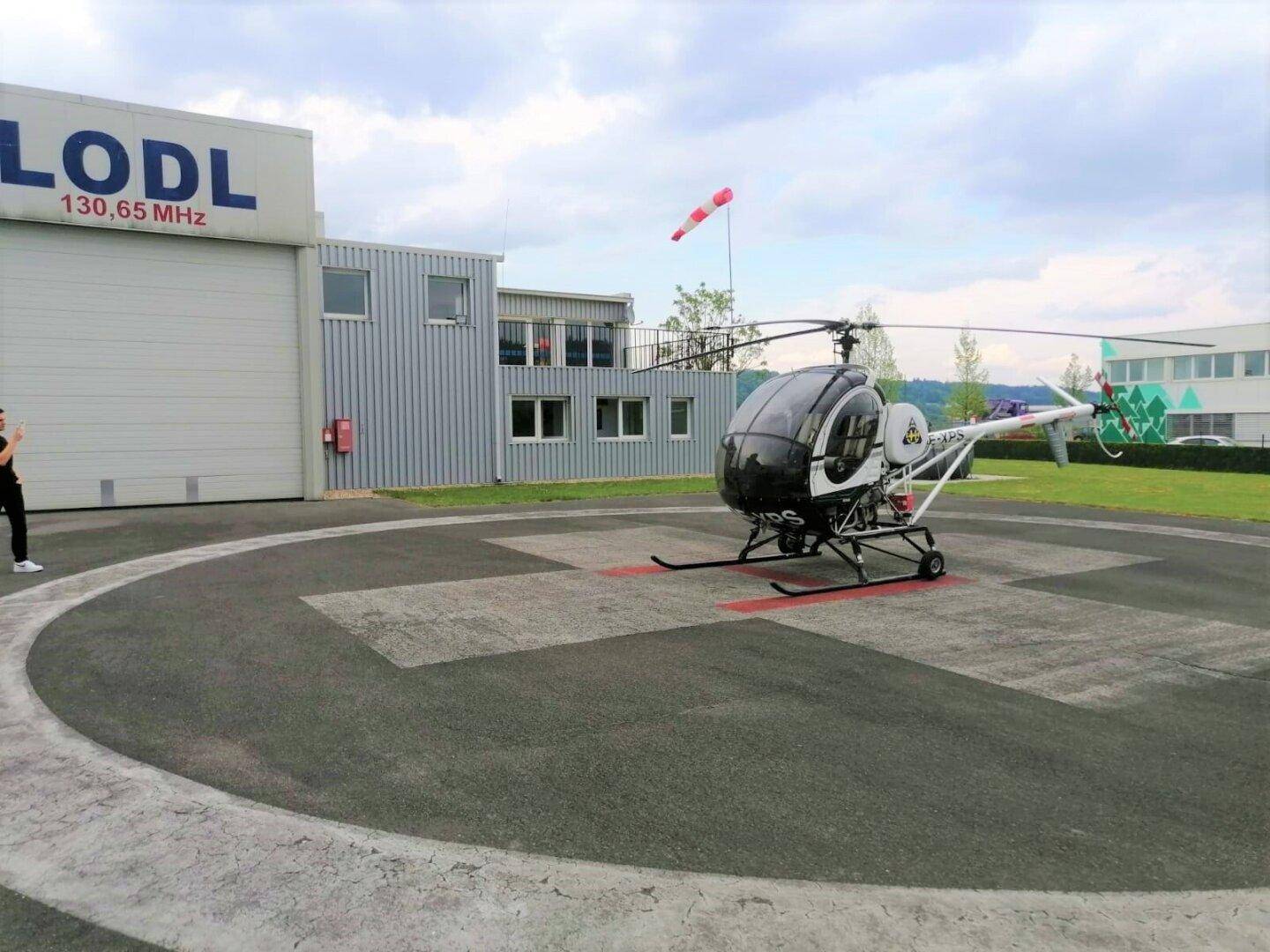 Ein Hubschrauber steht auf einem Landeplatz vor einem modernen Gebäude mit der Aufschrift "LODL".