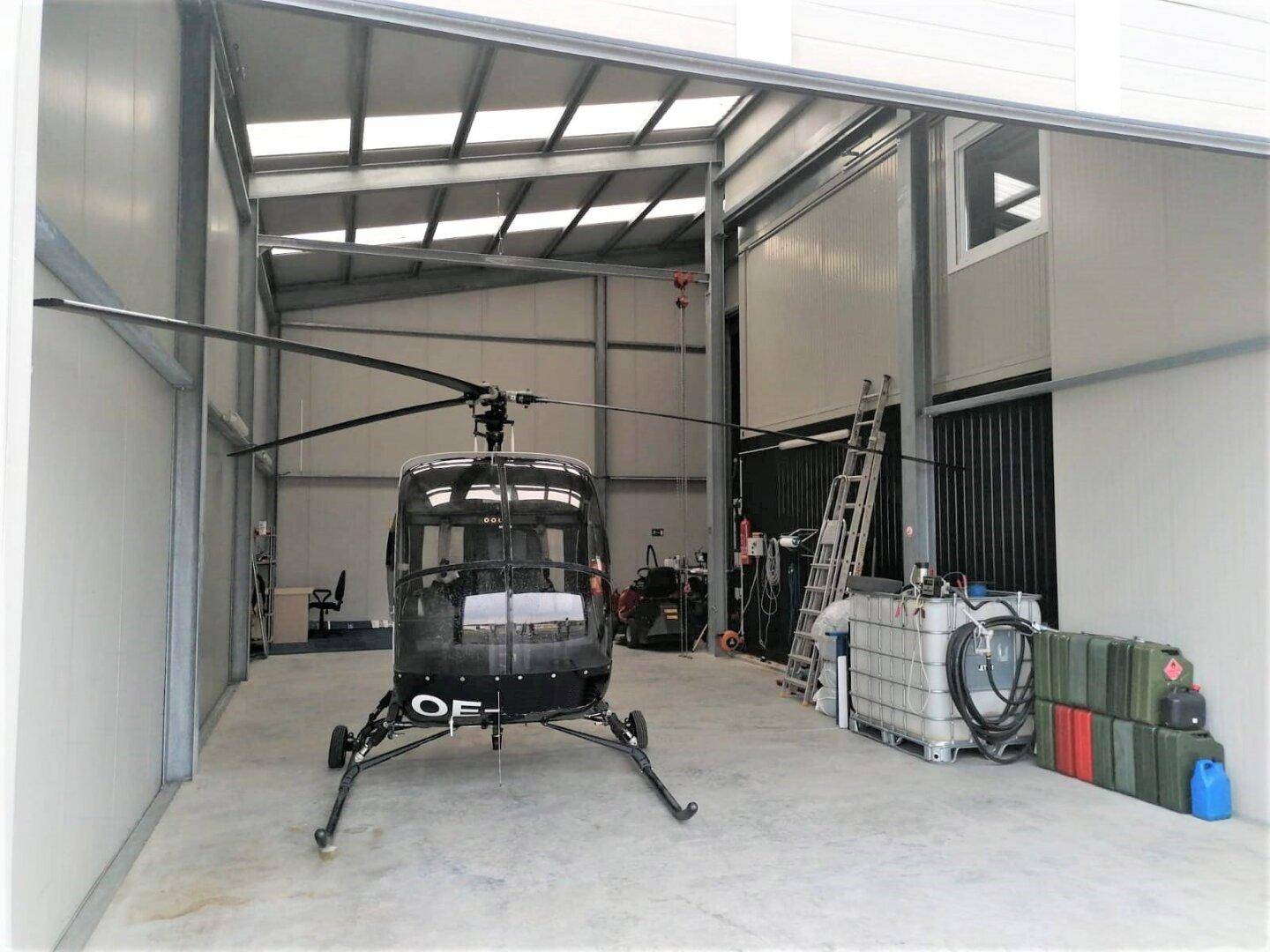 Ein geräumiger Hangar oder Lagerraum mit einem Hubschrauber, Metallregalen und Industrieböden.
