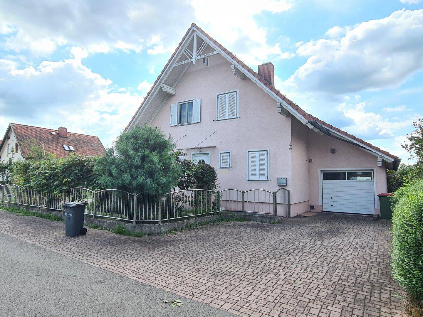 Vorderansicht eines Einfamilienhauses mit Garage, gepflasterter Einfahrt und weiß gestrichenen Fensterläden.