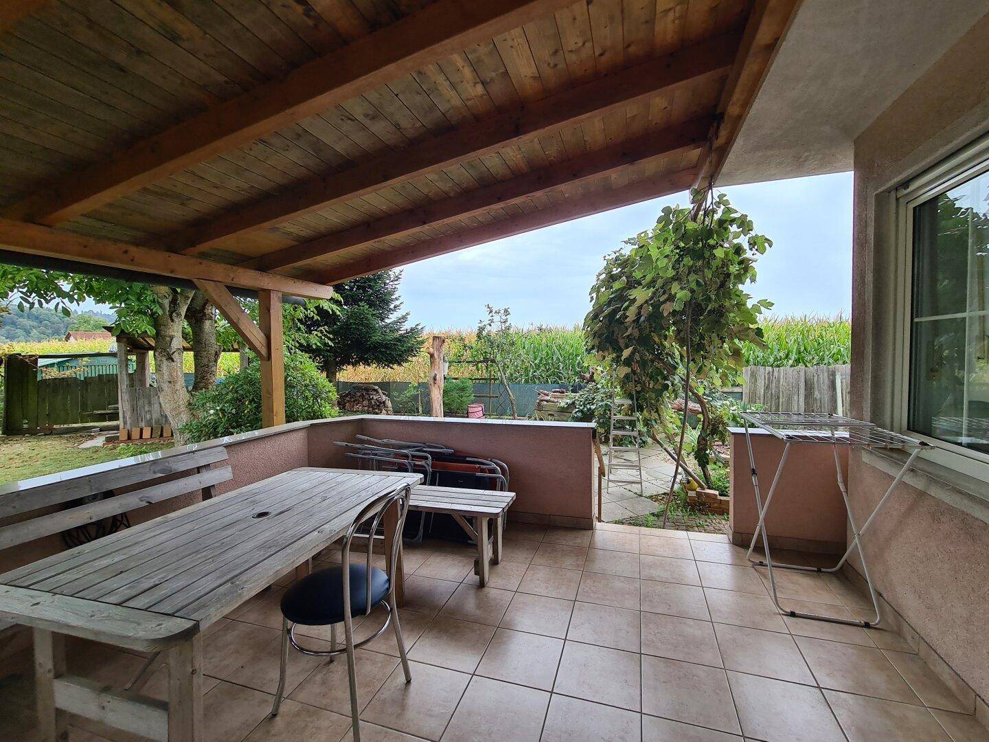 Geräumige überdachte Terrasse mit Holzdach und Blick auf den Garten und die Felder.