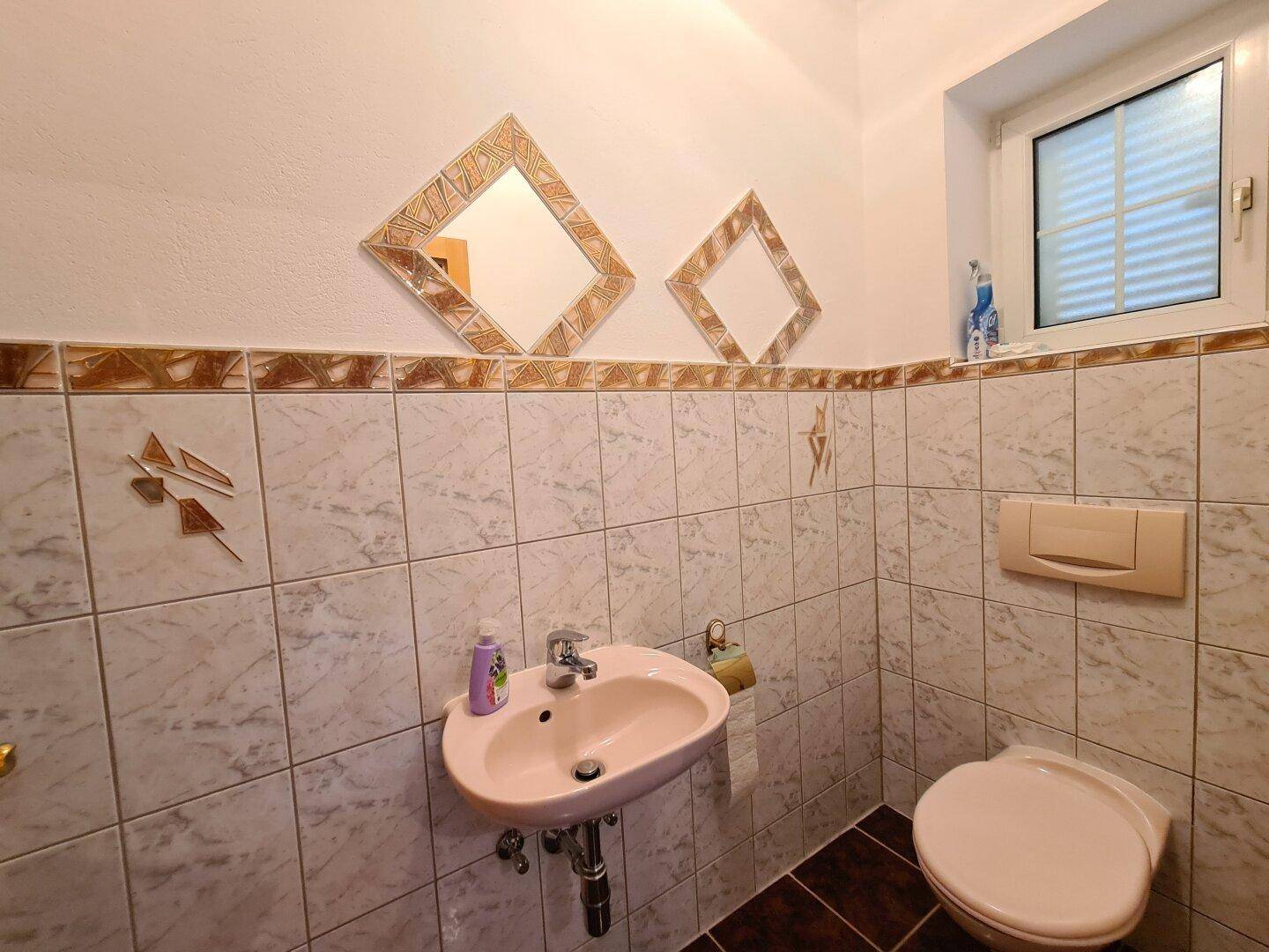 Kleines Gäste-WC mit Fenster, Wand-WC und dekorativen Fliesen.
