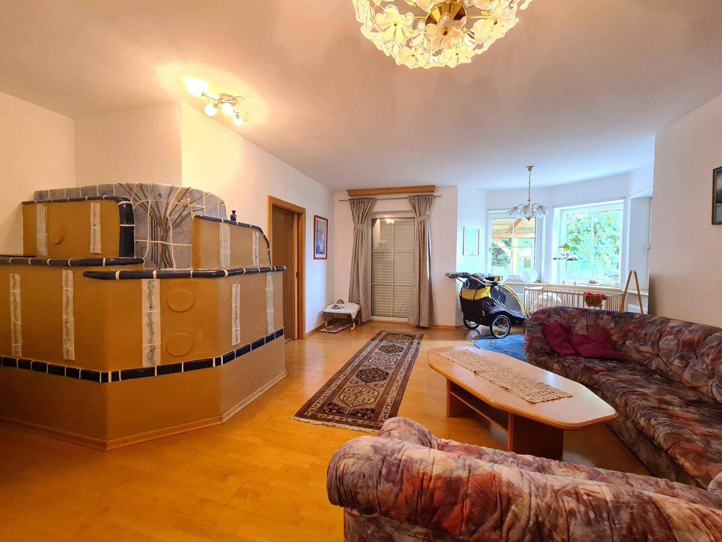 Gemütliches Wohnzimmer mit traditionellem Kachelofen, Parkettboden und Blick in den Garten.