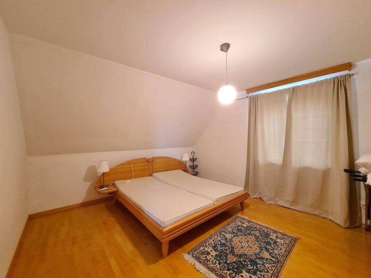 Schlafzimmer im Dachgeschoss mit Holzbett, Parkettboden und schrägen Wänden.