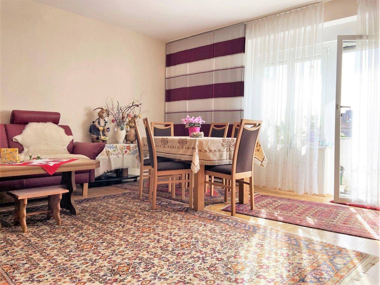 Gemütlicher Wohn-Essbereich mit Esstisch, Sofa und Zugang zum Balkon durch große Fenster, hell und einladend.