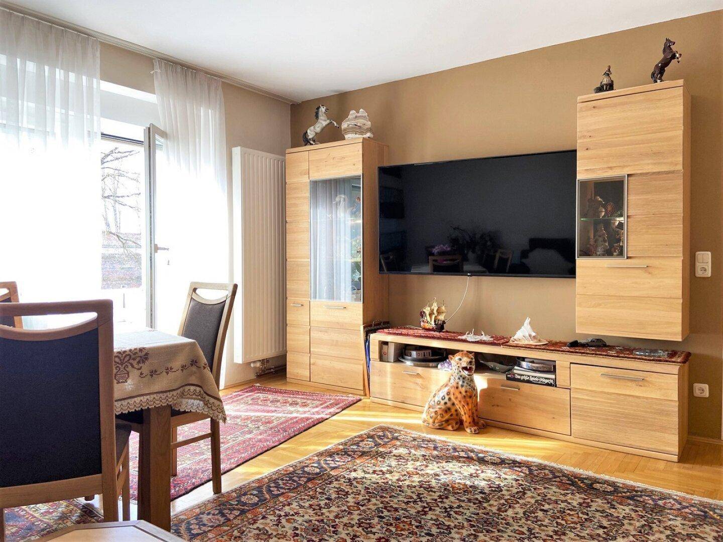 Wohnzimmer mit TV-Möbeln aus hellem Holz und Teppichboden, hell durch Fenster und modern eingerichtet.