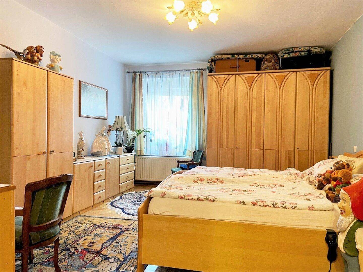 Schlafzimmer mit großem Holzkleiderschrank, Doppelbett und Teppich auf Parkettboden, gemütlich gestaltet.