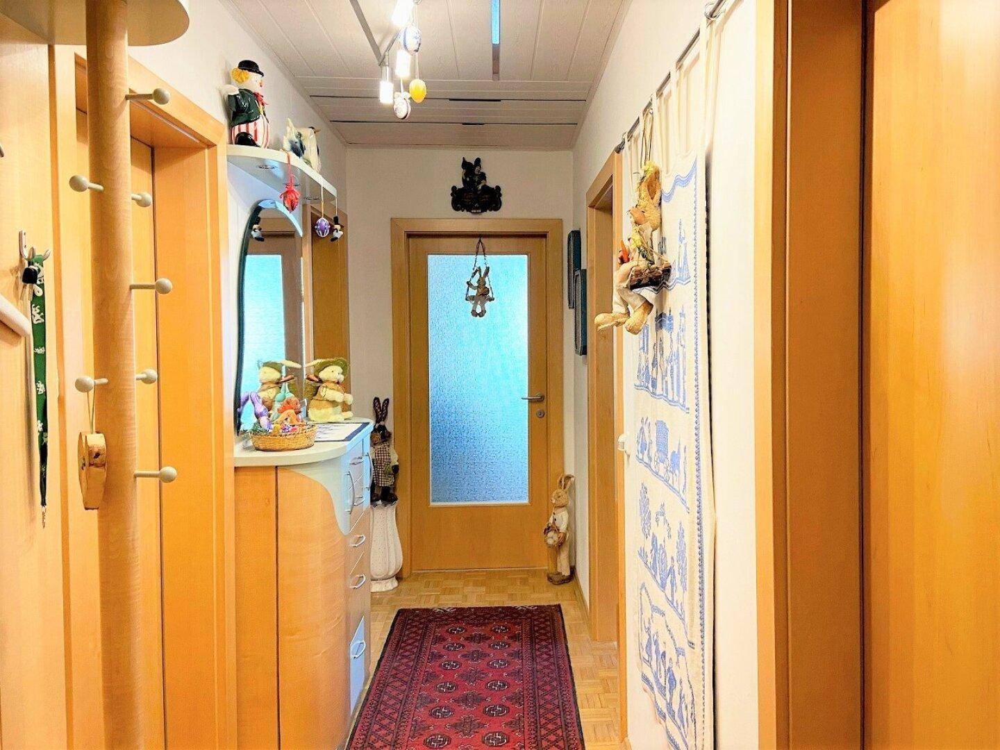 Heller Flur mit Holzverkleidung, Garderobe und Spiegel, freundlich dekoriert und gut beleuchtet.