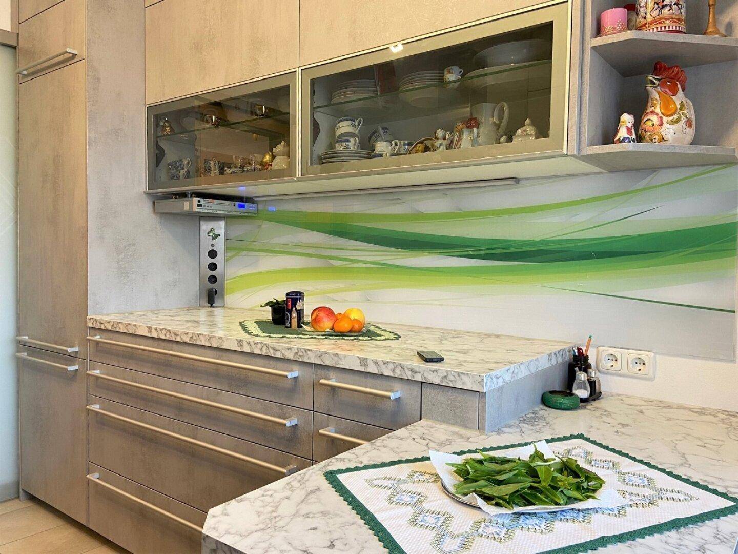 Moderne Küche mit hellen Schränken, Arbeitsplatten in Marmoroptik und grüner Spritzschutzwand.