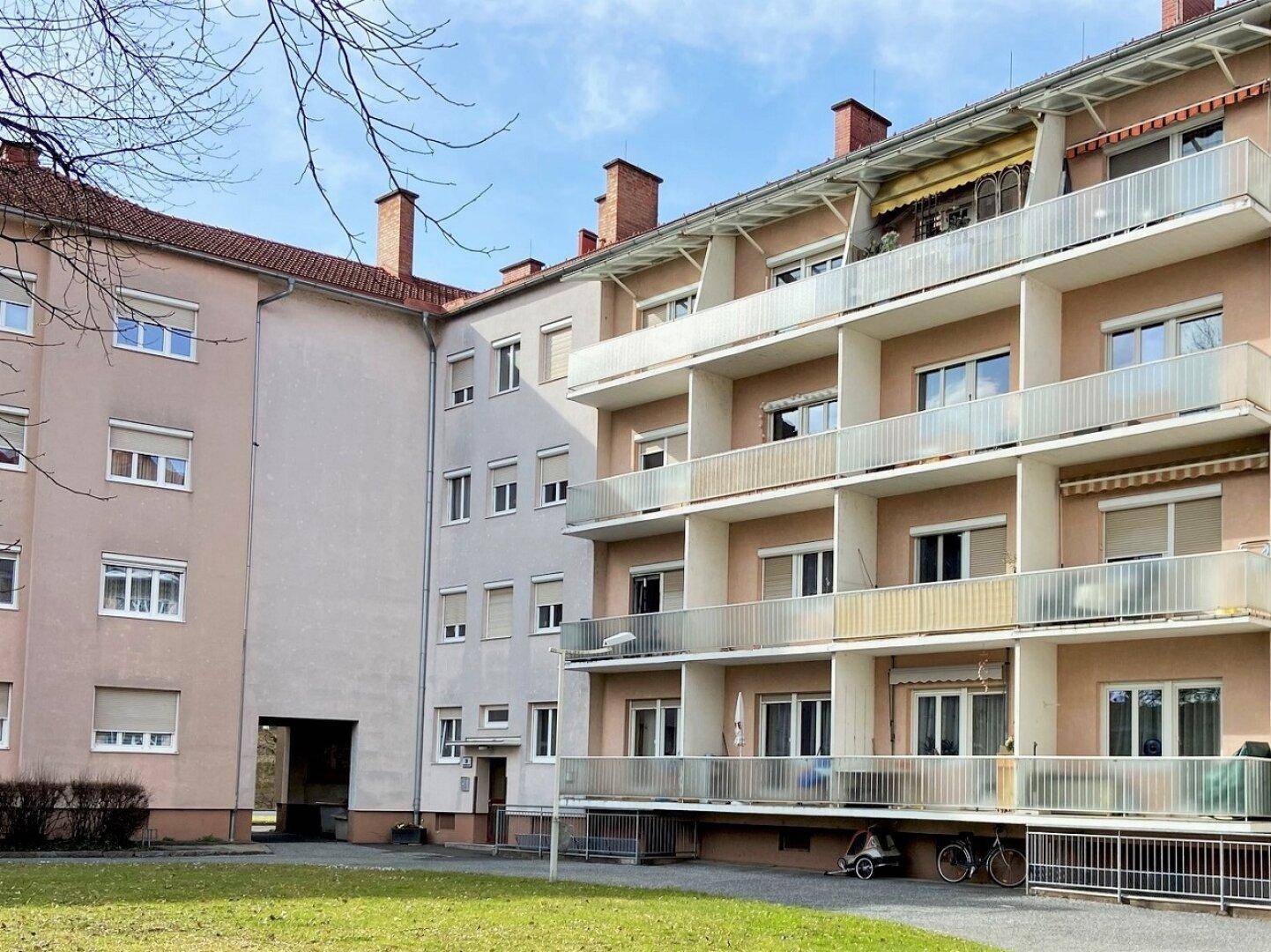 Mehrfamilienhaus mit mehreren Balkonen und einer gepflegten Grünfläche im Vordergrund, gut erhalten.