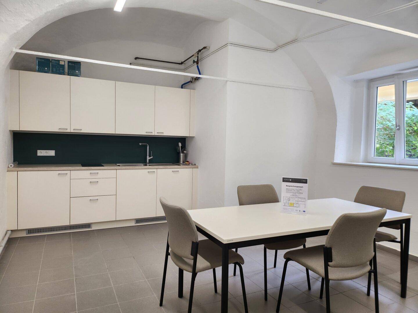 Funktionale Küche mit weißen Schränken, Esstisch und gewölbter Decke, ideal für Mitarbeiterpausen.