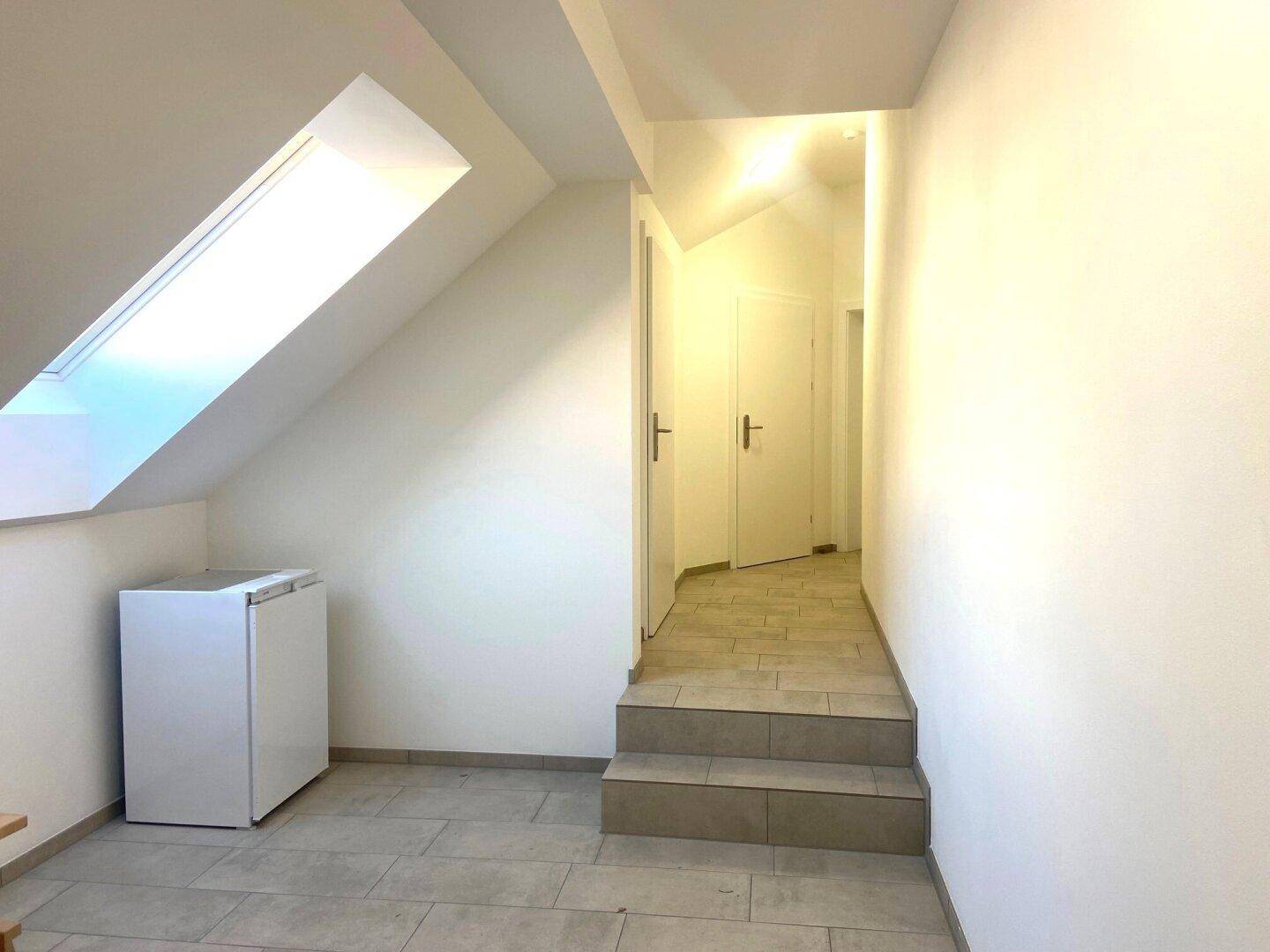 Heller Flur mit Dachfenster, Fliesenboden und einem kleinen Kühlschrank unter der Dachschräge.