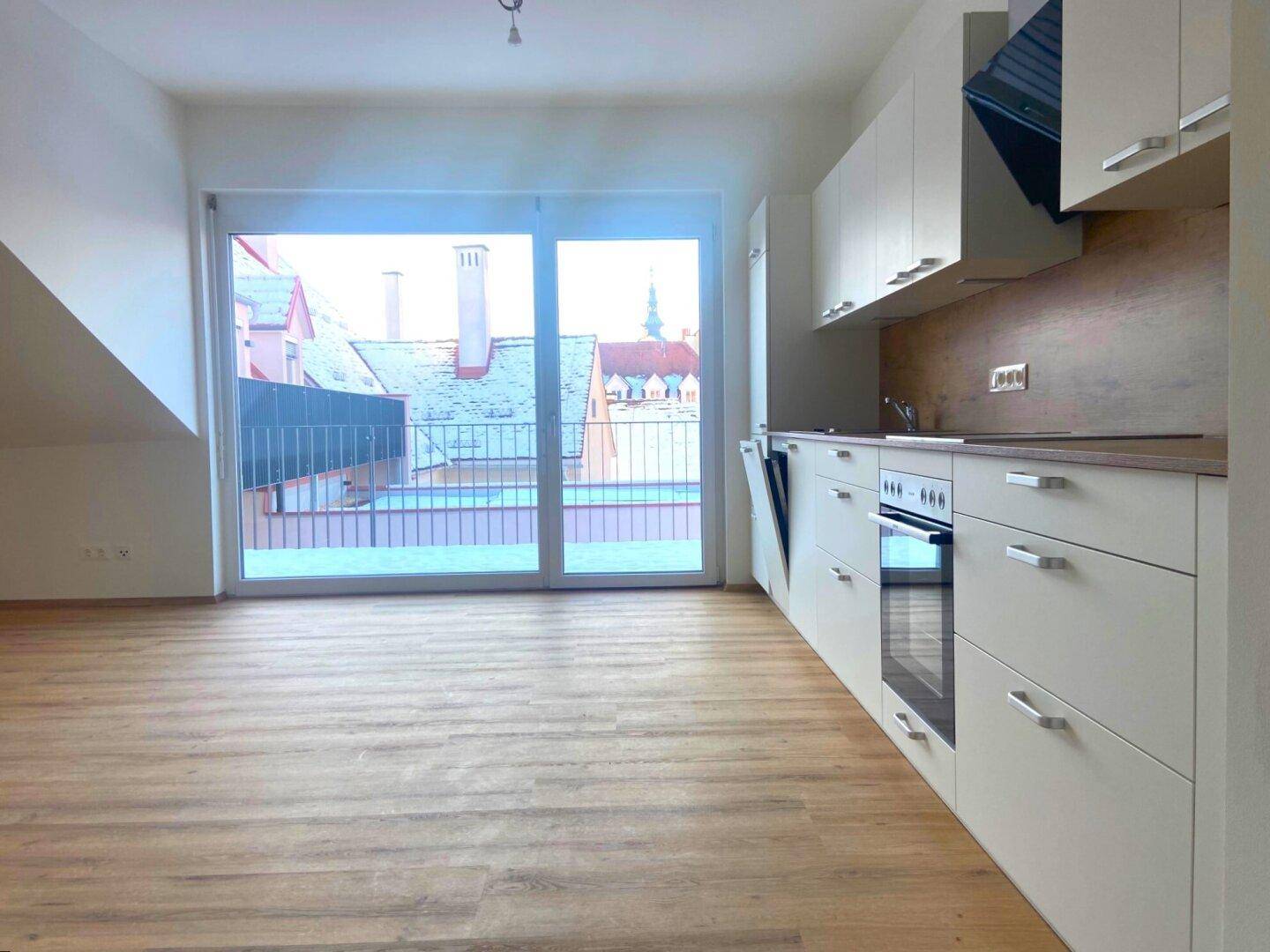 Helle Küche mit Einbaugeräten, Holzfußboden und Zugang zu einem Balkon oder einer Terrasse.