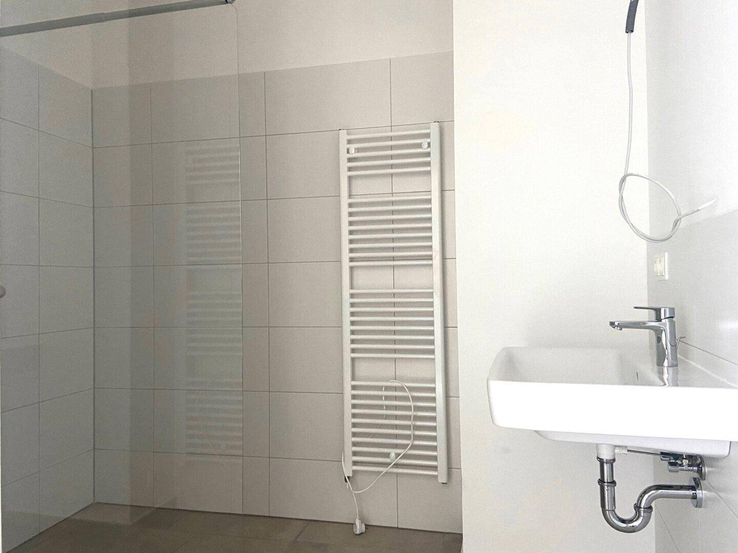 Modernes Badezimmer mit weißen Fliesen, Einzelwaschbecken und beheiztem Handtuchhalter.