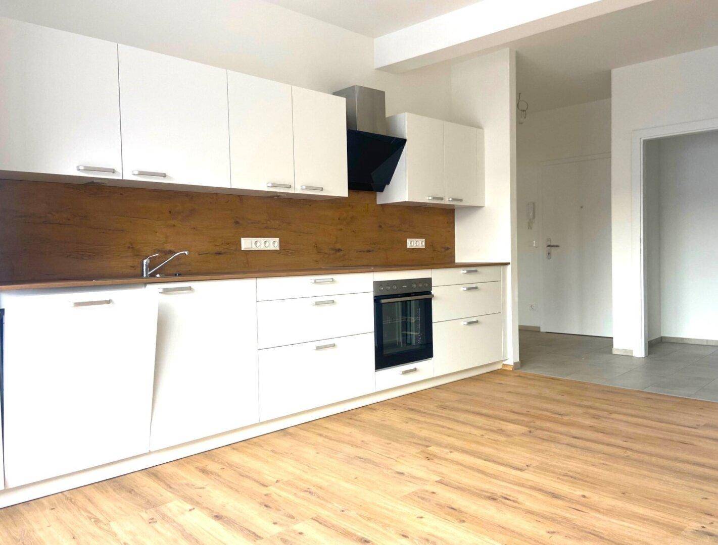 Neue Einbauküche mit weißen Schränken, Holzrückwand und modernem Laminatboden.