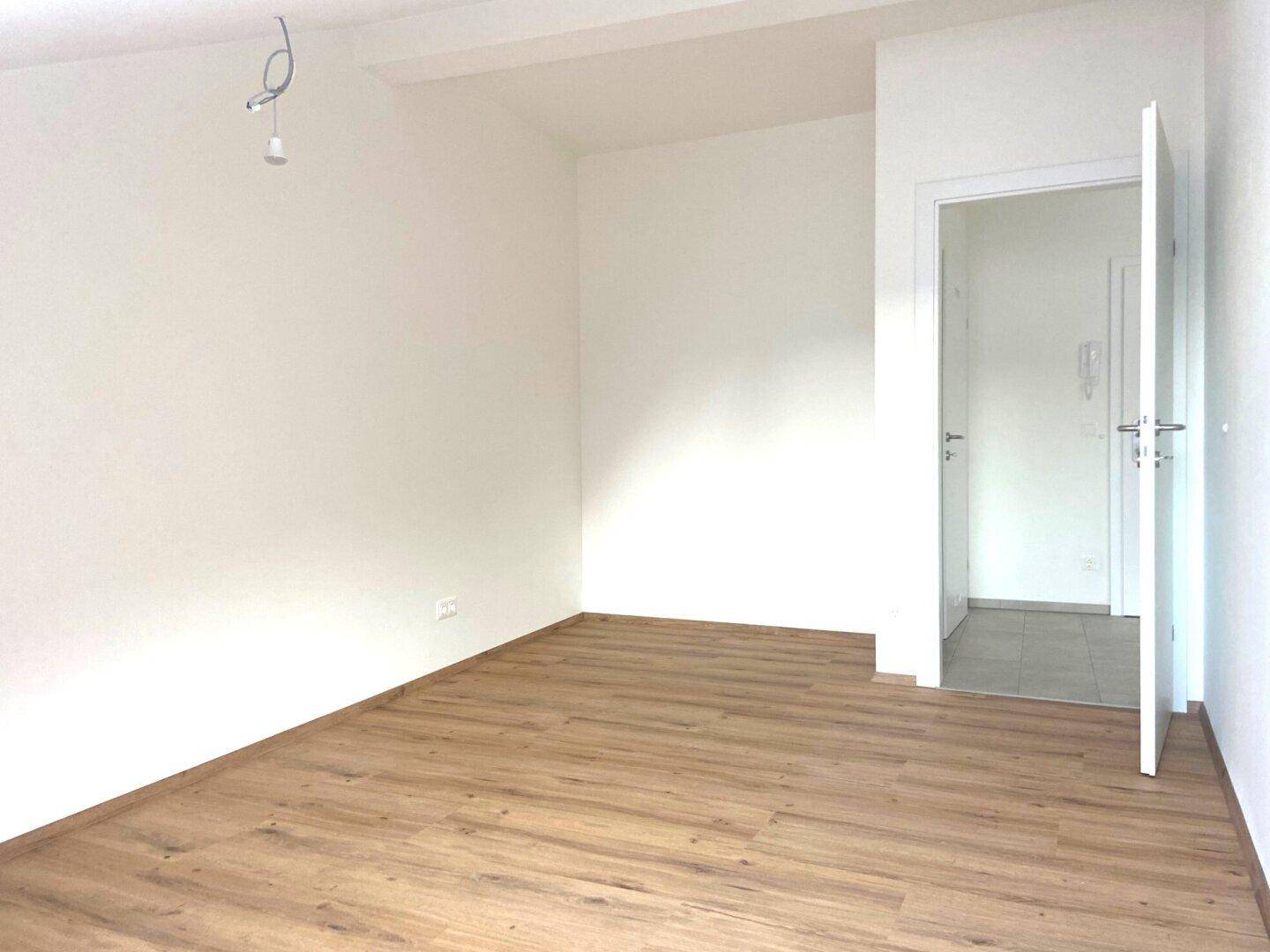 Leerer Raum mit hellem Laminatboden und weißen Wänden, bereit zur individuellen Gestaltung.