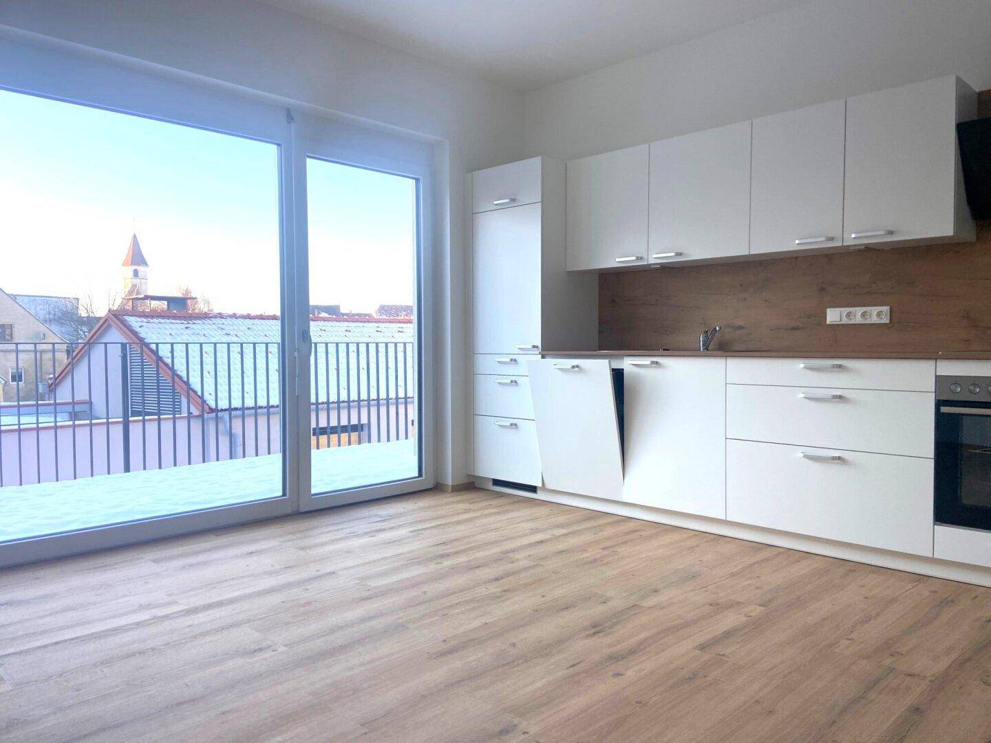 Moderne Küche mit weißen Schränken, Holzoptik-Rückwand und Zugang zu einem Außenbereich.
