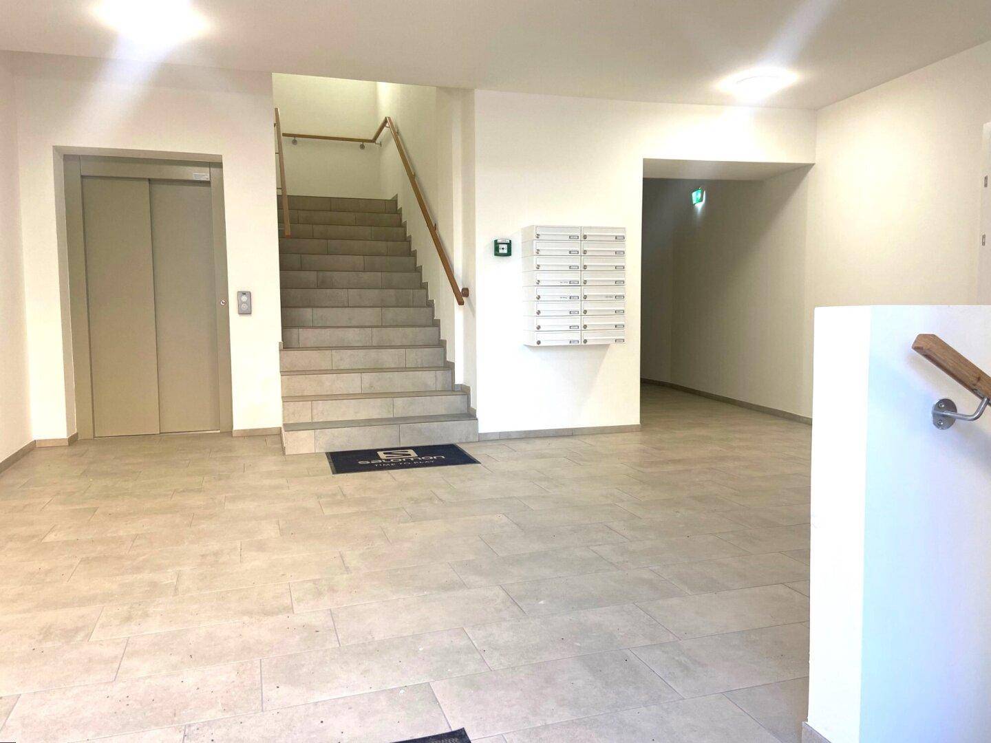 Heller Eingangsbereich mit Treppenhaus, Aufzug und Briefkästen in einem Mehrparteienhaus.