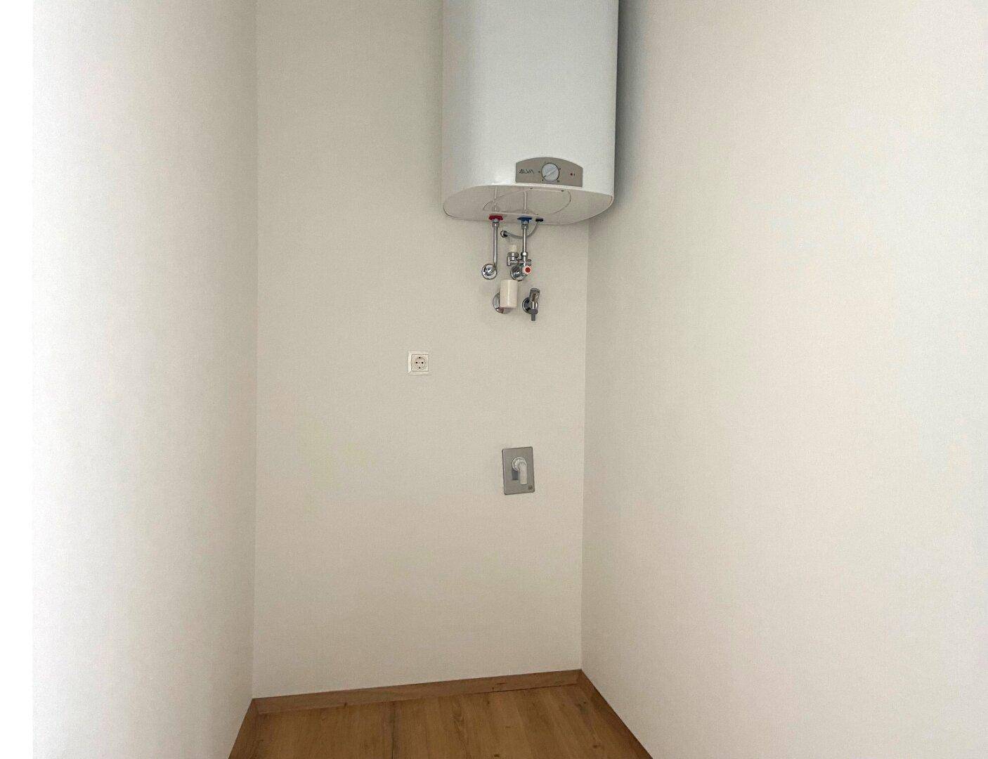 Praktischer Hauswirtschaftsraum mit Warmwasserboiler und Anschlüssen für Waschmaschine.