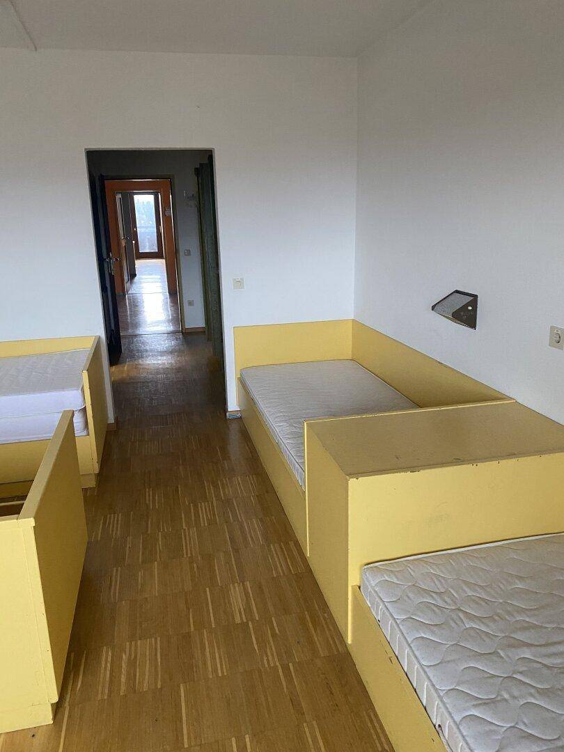Helles Mehrbettzimmer mit gelben Betten und Holzparkettboden, ideal für Wohngemeinschaften oder Gäste.