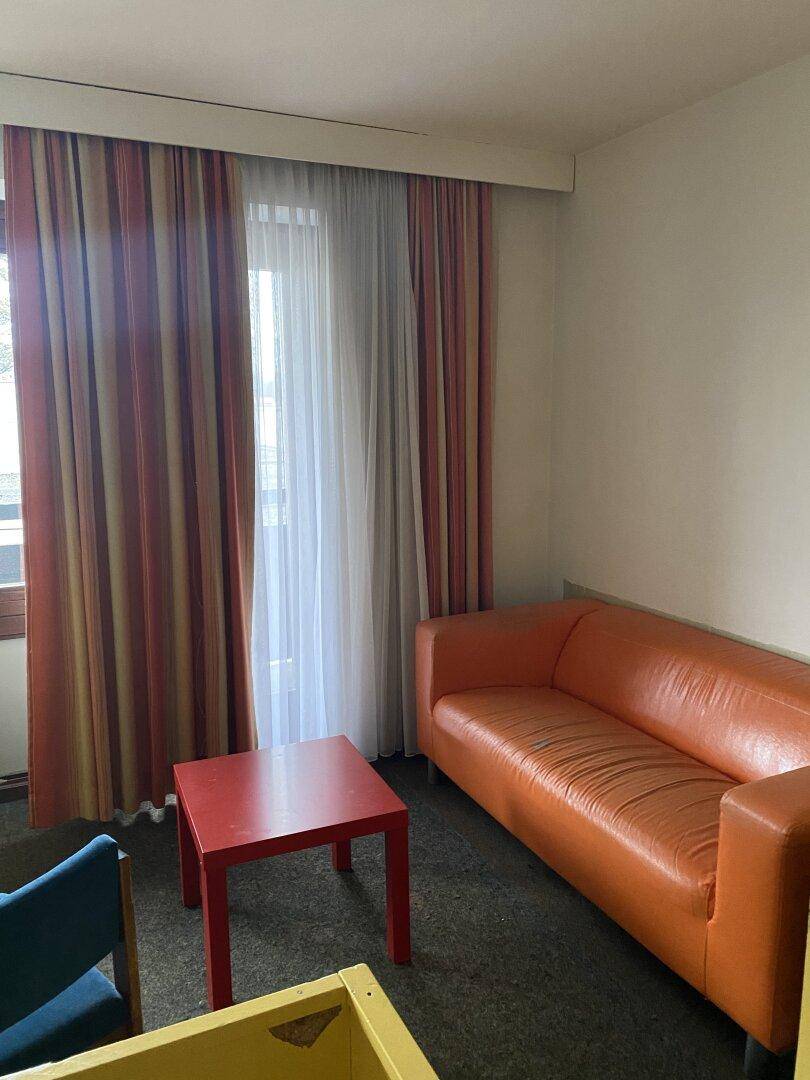 Gemütliches Zimmer mit orangefarbenem Sofa, kleinem roten Tisch und Fenster mit Vorhängen.