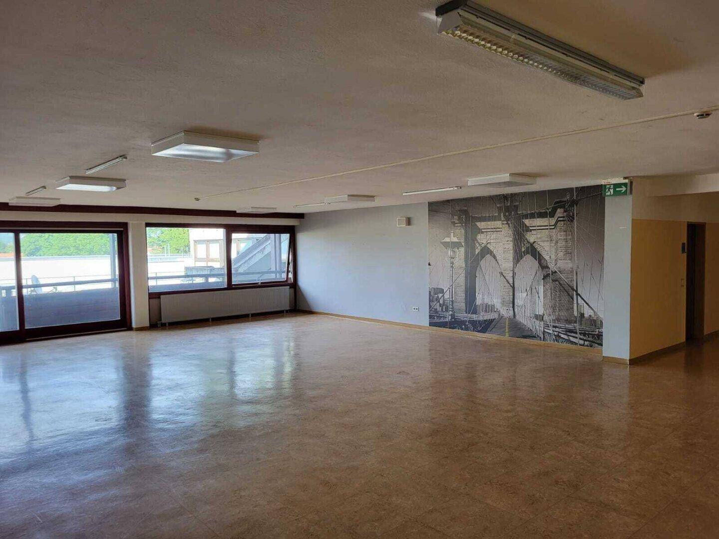 Heller, weitläufiger Raum mit einer Wanddekoration der Brooklyn Bridge und großen Fenstern mit Zugang zu einem Balkon.