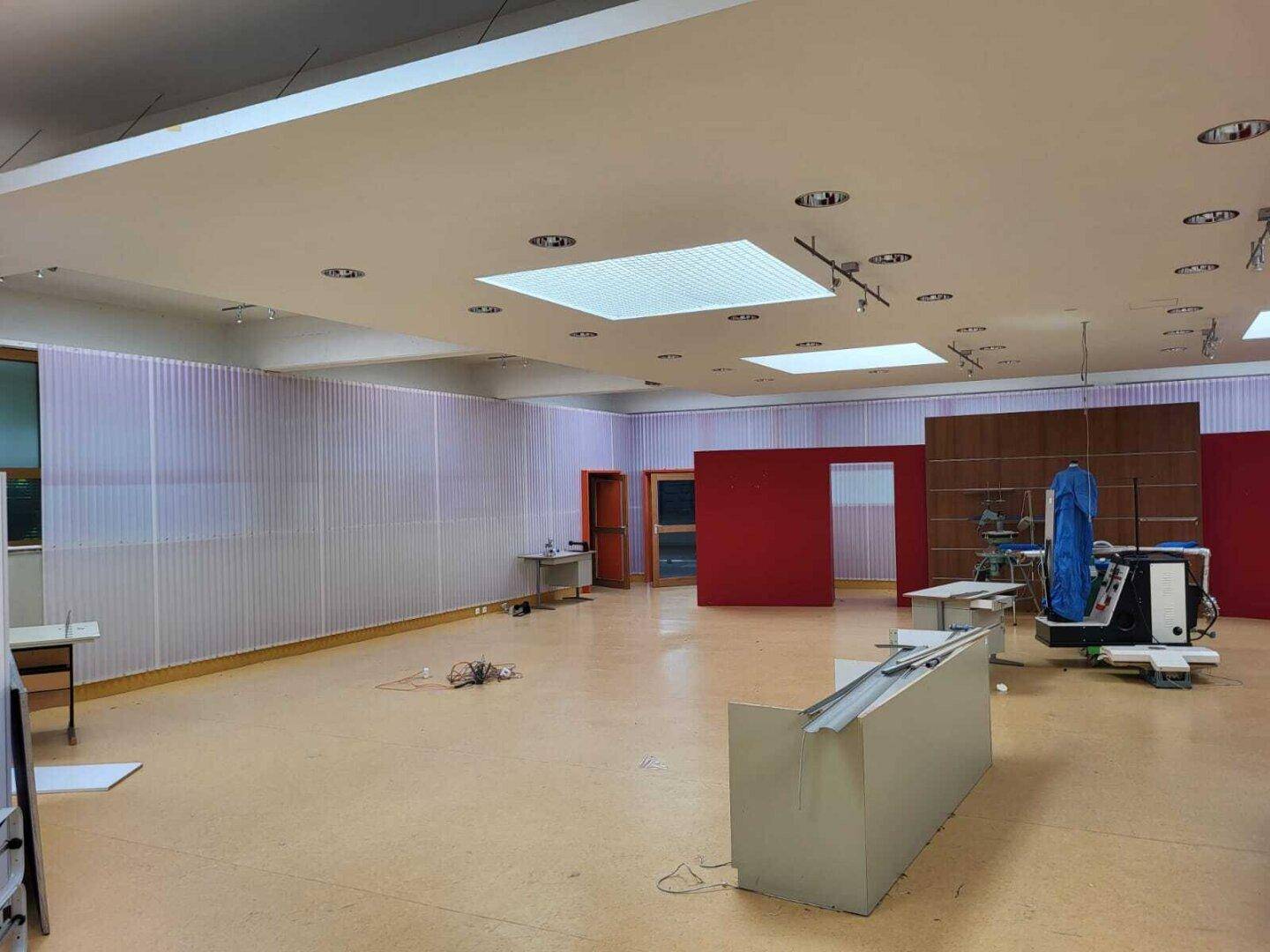 Großer, heller Verkaufsraum mit modernen Deckenleuchten, roten Akzentwänden und transluzenten Trennwänden.
