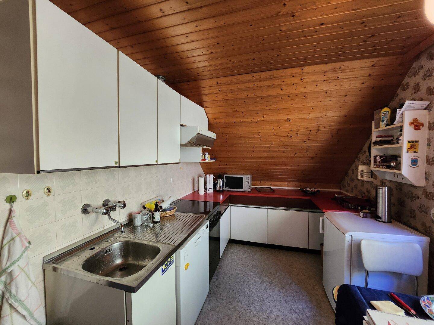 Einfache Küche mit Dachschräge, weißen Schränken und Holzdecke.