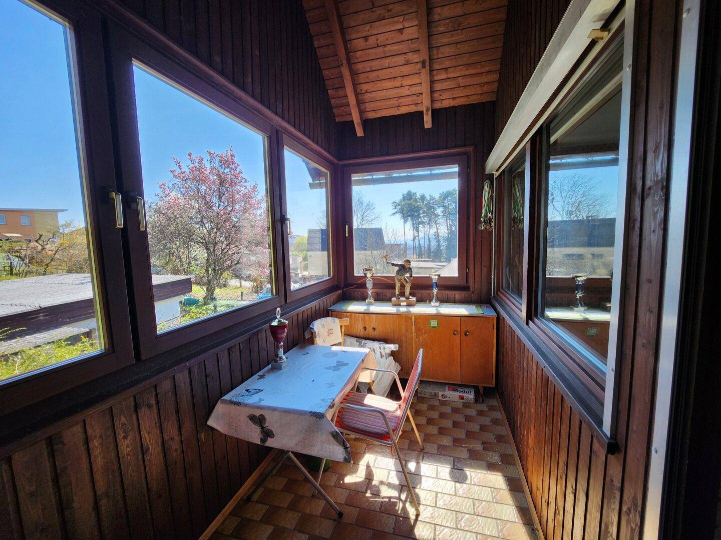 Verglaster Balkon oder Wintergarten mit Holzverkleidung, Fliesenboden und weitem Ausblick.
