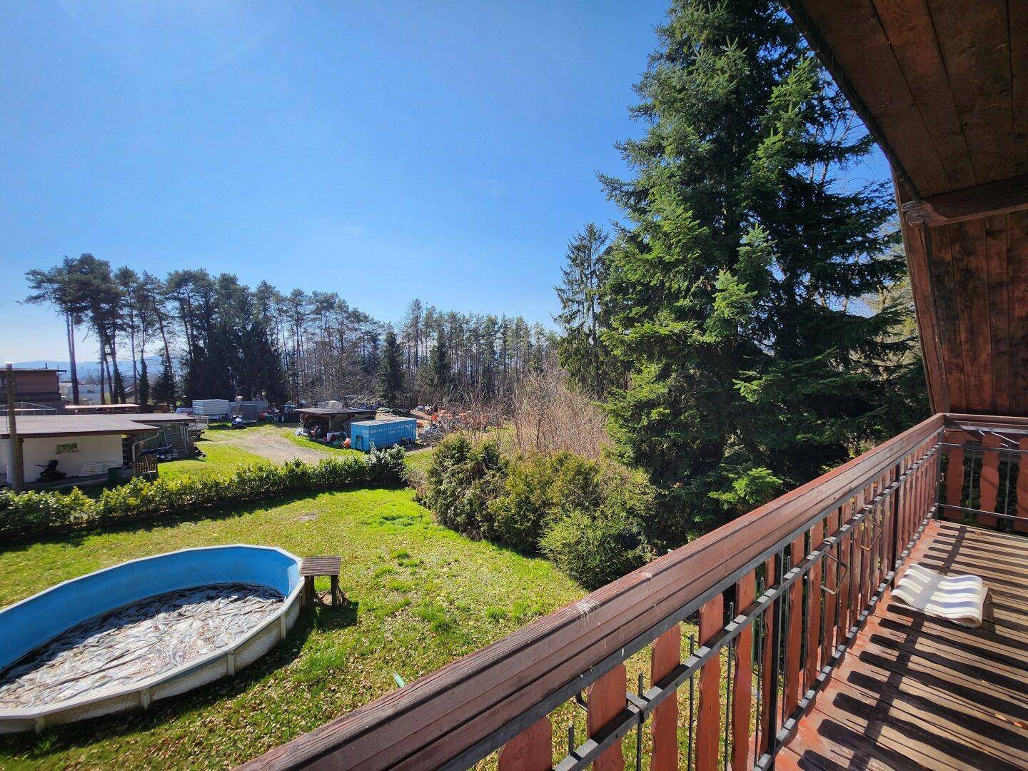 Blick vom Balkon auf den Garten mit Aufstellpool und die umliegende grüne Landschaft.