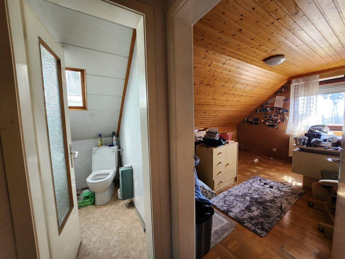 Kleines WC mit Dachschräge und angrenzendem Zimmer mit Holzboden.