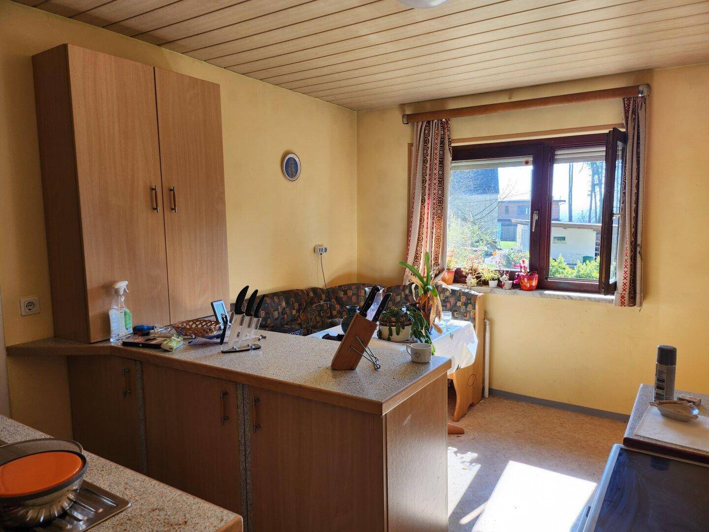 Funktionale Küche mit Holzschränken, Essbereich und einem Fenster mit Blick ins Grüne.