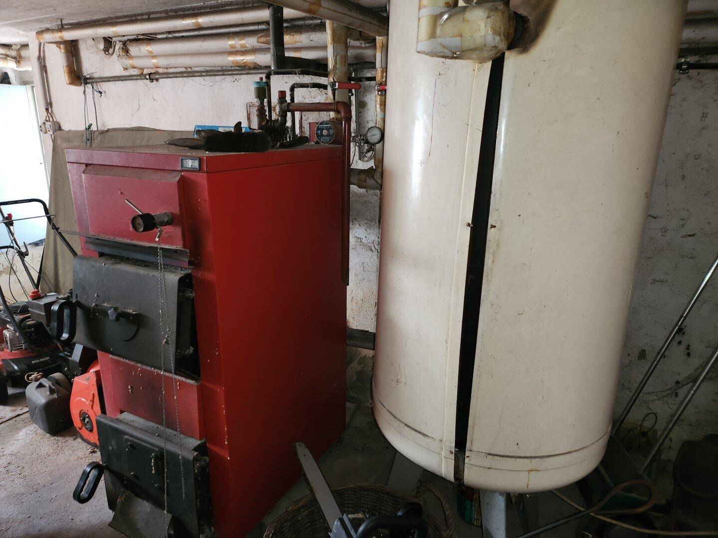 Heizungsraum im Keller mit einem großen roten Heizkessel und einem Warmwasserspeicher.