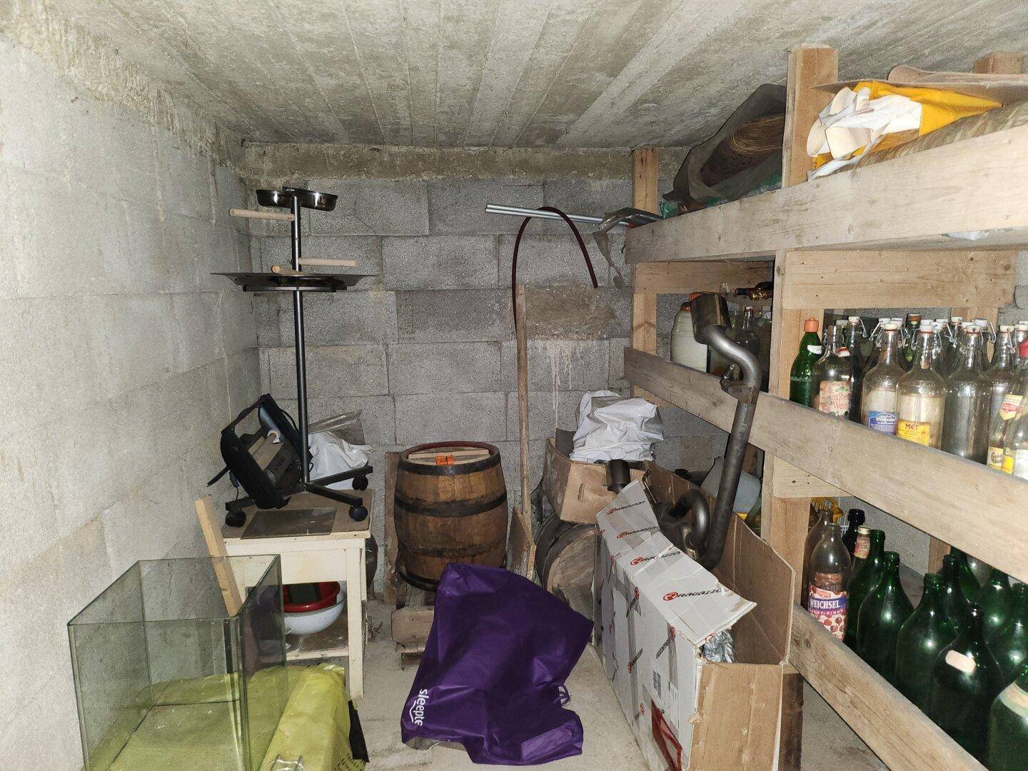 Kellerraum mit Betonwänden, Holzregalen und verschiedenen gelagerten Gegenständen.