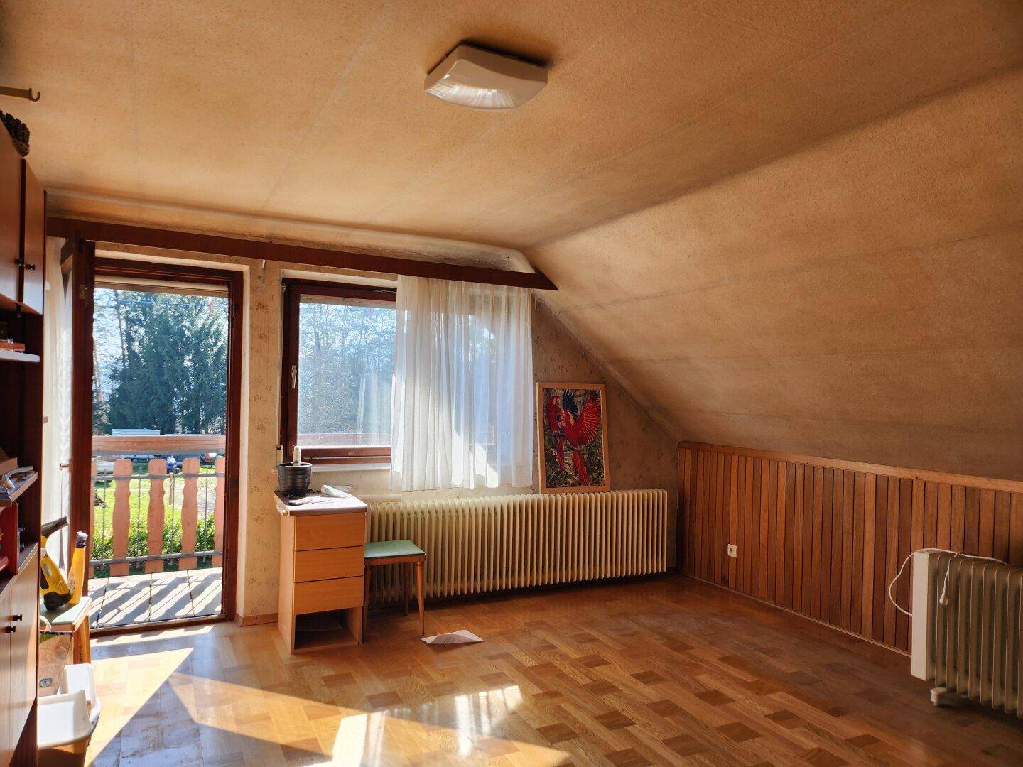 Helles Schlafzimmer mit Holzboden, Dachschräge und Zugang zu einem Balkon.