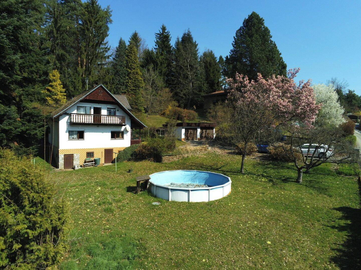 Gartenbereich mit einem Aufstellpool, umgeben von Bäumen und blühenden Sträuchern.