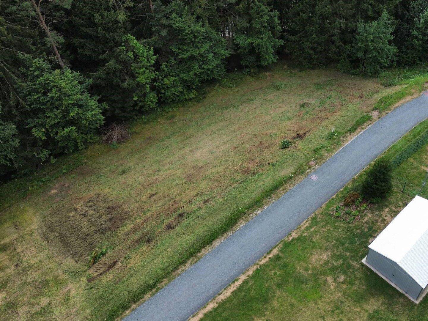 Nahaufnahme des Grundstücks von oben, umgeben von Wald und einer asphaltierten Straße.