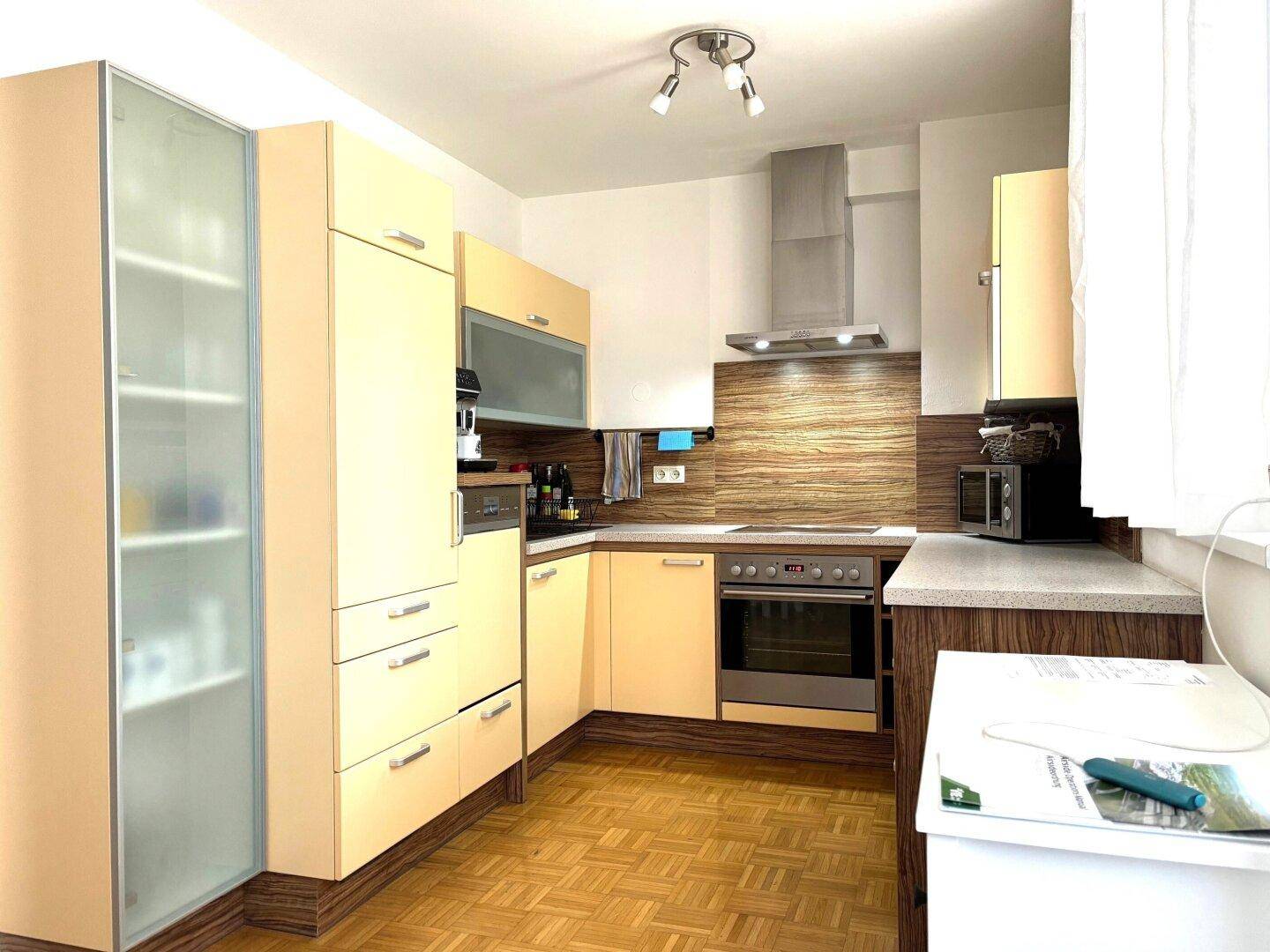 Funktionale Küche mit hellen Einbauschränken, Parkettboden und integrierten Geräten.