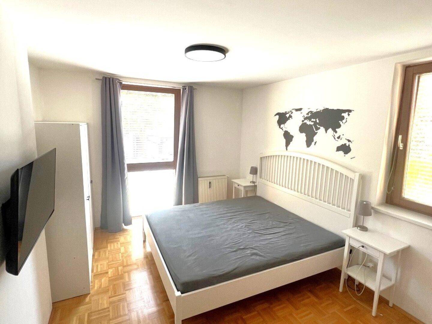 Helles Schlafzimmer mit Doppelbett, Parkettboden und dekorativer Weltkarte an der Wand.