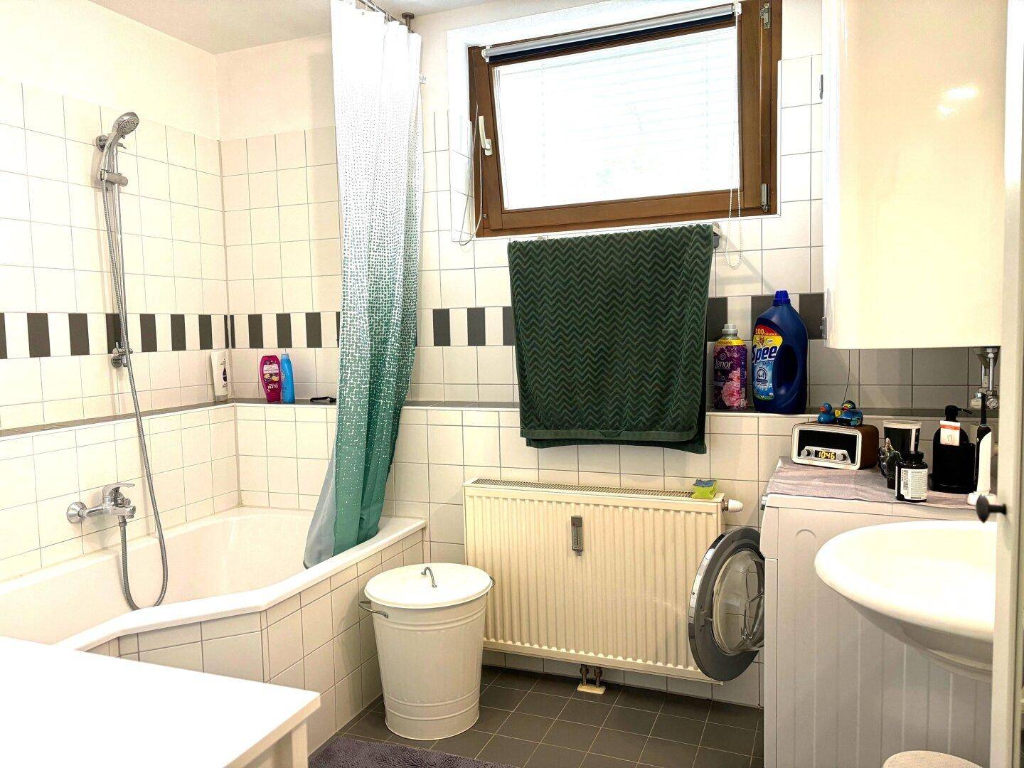 Badezimmer mit Badewanne, Duschvorhang, Waschmaschine und Fenster für natürliche Belüftung.